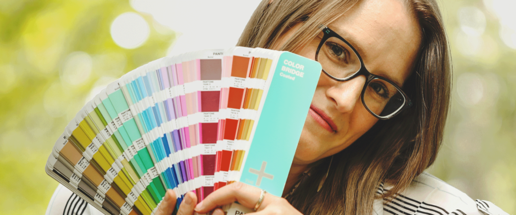 Kara Israel owner of TalaKamora Design LLC holding up a Pantone book. She provides web and graphic design services in central Illinois.